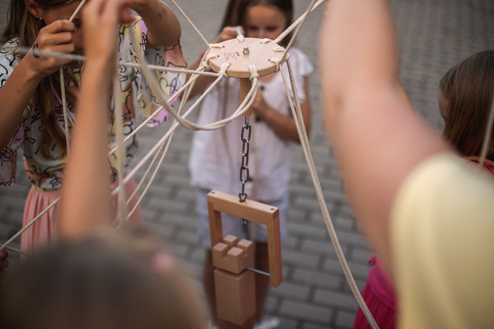 Gra zespołowa dla dzieci z drewnianą konstrukcją i linami, angażująca kilka osób. Element integracyjny na imprezie plenerowej z bliska.