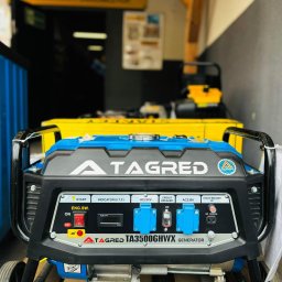 MDM GROUP SPÓŁKA Z OGRANICZONĄ ODPOWIEDZIALNOŚCIĄ SPÓŁKA KOMANDYTOWA - Agregat prądotwórczy Tagred TA3500GHWX na drewnianej palecie, z widocznymi gniazdami AC230V i zabezpieczeniami obwodów, ustawiony w magazynie.