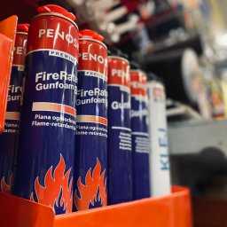MDM GROUP SPÓŁKA Z OGRANICZONĄ ODPOWIEDZIALNOŚCIĄ SPÓŁKA KOMANDYTOWA - Półka z puszkami piany ogniochronnej Penos FireRate Gunfoam w markecie budowlanym, widoczne etykiety z płomieniami i napisem 'Piana ogniochronna'.