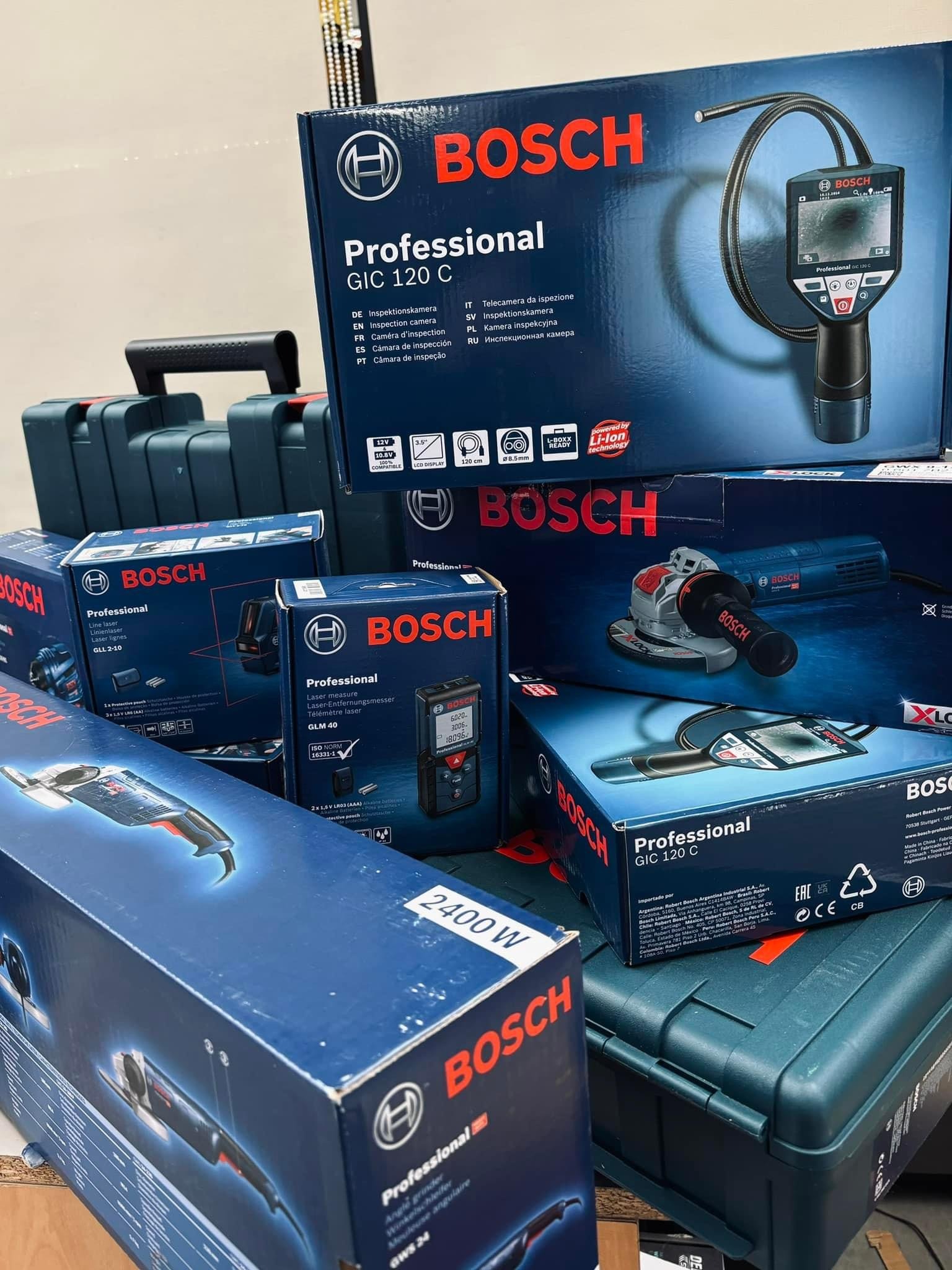 Zestaw zapakowanych elektronarzędzi marki Bosch Professional, w tym szlifierka kątowa, kamera inspekcyjna GIC 120 C, dalmierz laserowy GLM 40, w pudełkach i walizkach transportowych.