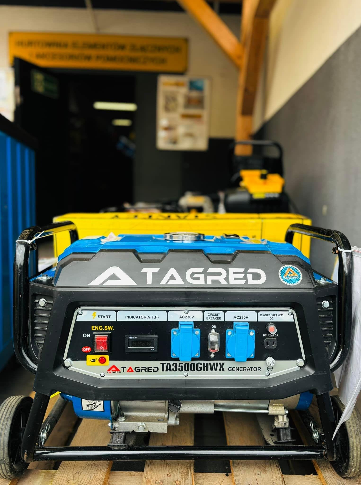 Agregat prądotwórczy Tagred TA3500GHWX na drewnianej palecie, z widocznymi gniazdami AC230V i zabezpieczeniami obwodów, ustawiony w magazynie.