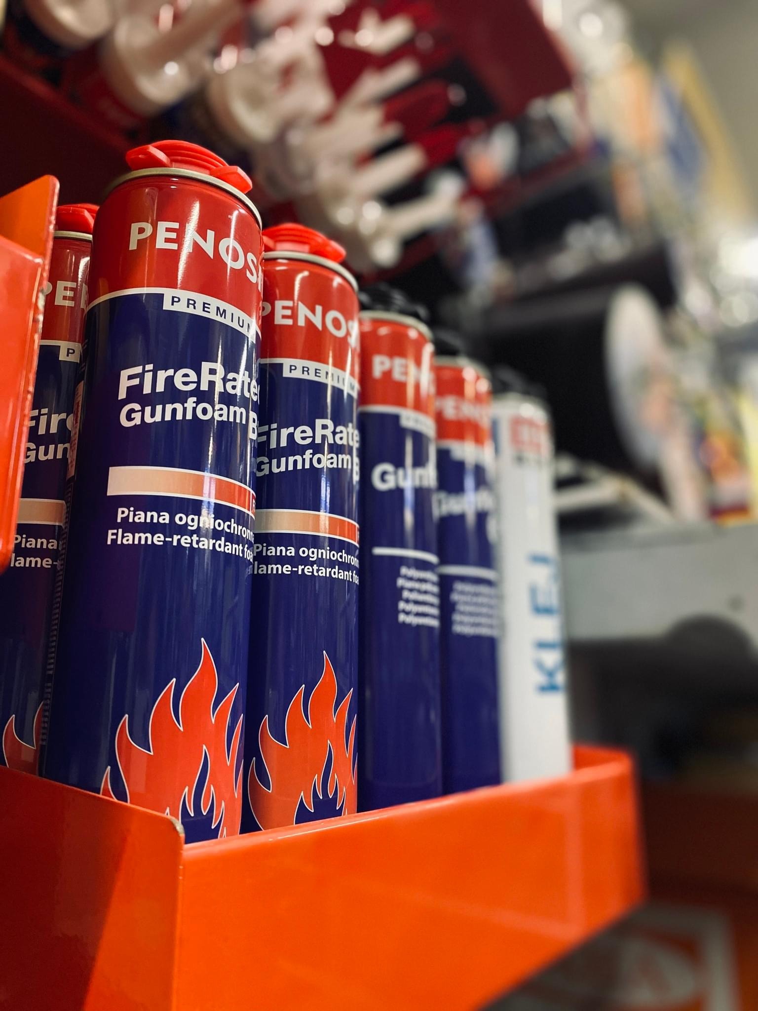 Półka z puszkami piany ogniochronnej Penos FireRate Gunfoam w markecie budowlanym, widoczne etykiety z płomieniami i napisem 'Piana ogniochronna'.