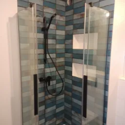 Kabina prysznicowa z niebiesko-szarą mozaiką ułożoną w jodełkę, czarna armatura i wnęki na kosmetyki.