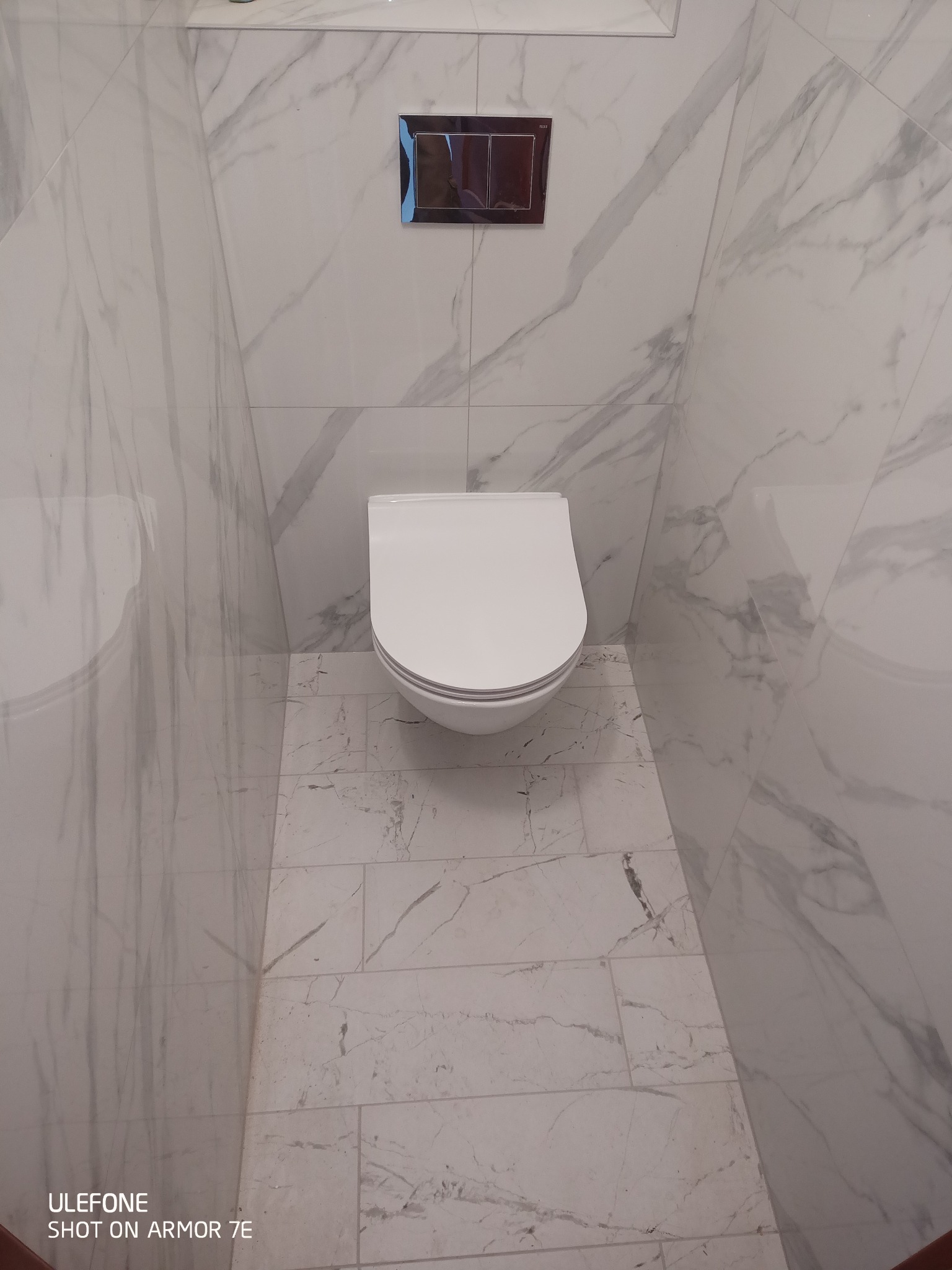 Nowoczesna toaleta podwieszana w łazience wykończonej białymi płytkami imitującymi marmur, widok z góry na minimalistyczny design.