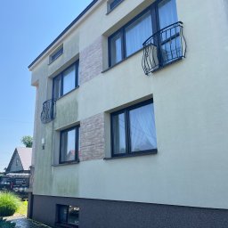 Winclear mycie okien i elewacji - Trzypiętrowy budynek z jasną elewacją, fragmentami wyczyszczonymi i balkonami z ozdobnymi balustradami, widoczny wąż do mycia elewacji przy chodniku.