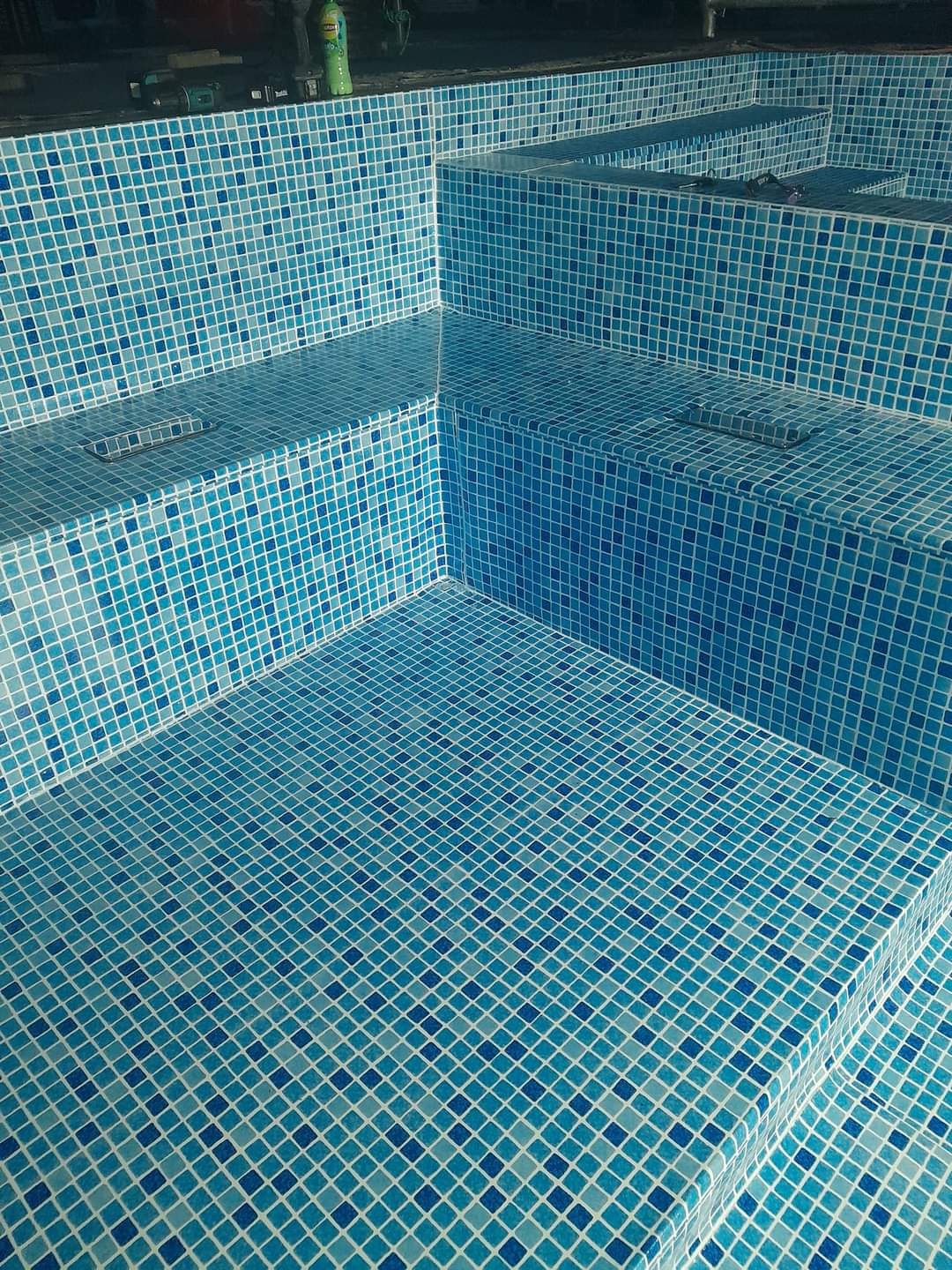 Stopnie w basenie wyłożone mozaiką w odcieniach błękitu i turkusu, z widocznym odpływem liniowym na jednym ze stopni.