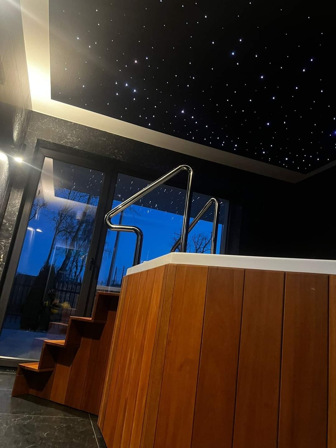 Kryty basen z drewnianą obudową, chromowanymi poręczami i schodami; sufit imitujący rozgwieżdżone niebo.