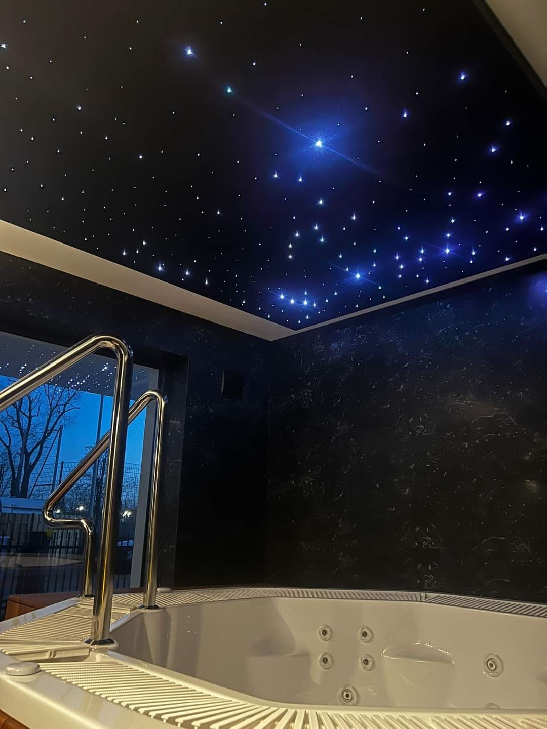 Wanna z hydromasażem w pomieszczeniu z dekoracyjnym oświetleniem sufitowym imitującym rozgwieżdżone niebo.