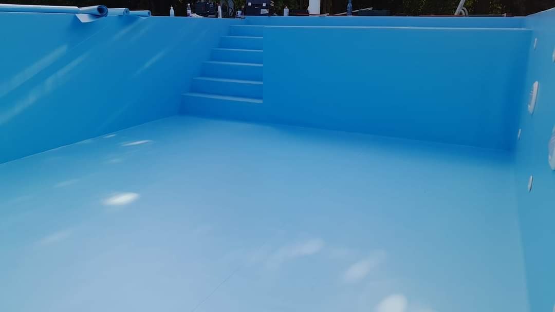 Wnętrze niebieskiego basenu z wbudowanymi schodami, widoczne rolki folii na krawędzi, przygotowane do wykończenia.