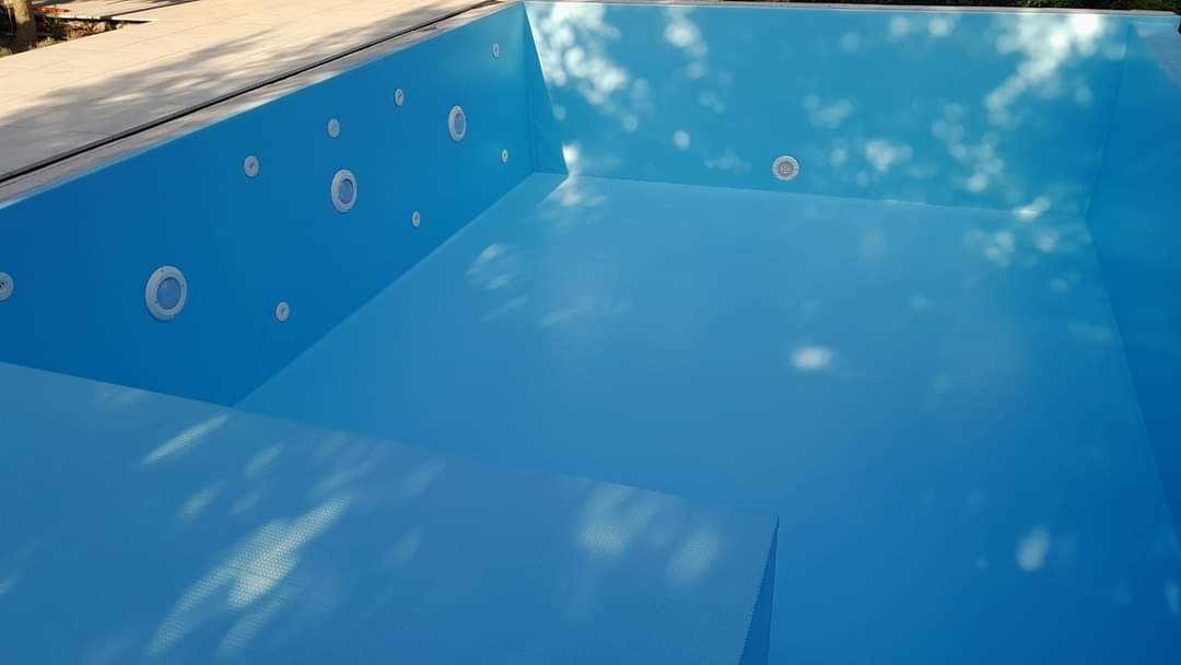 Pusty, wyłożony niebieską folią, prostokątny basen w trakcie budowy lub renowacji, z zamontowanymi dyszami i schodkami, widoczne refleksy światła na dnie.