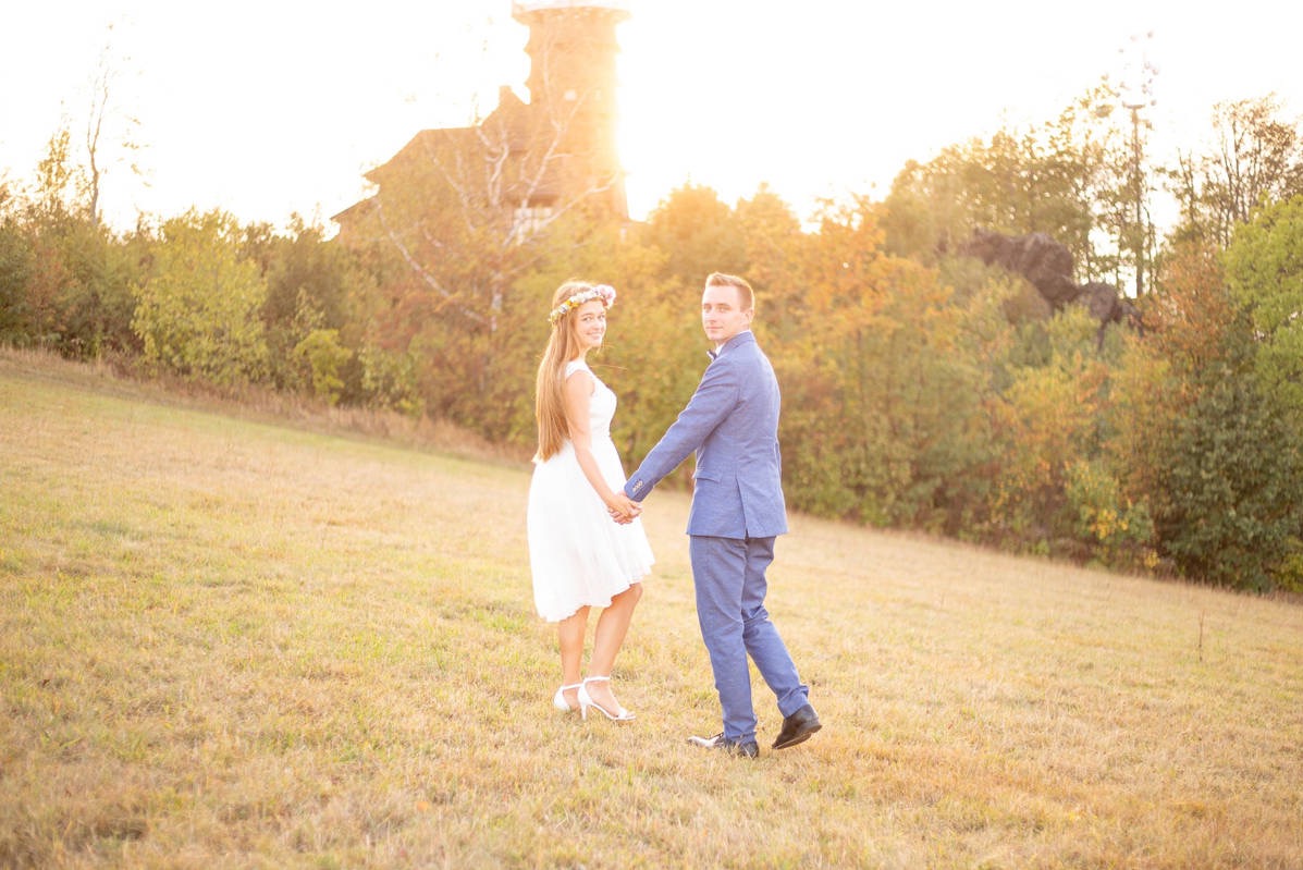 Para młoda trzymająca się za ręce na tle drewnianej wieży widokowej w jesiennej scenerii.