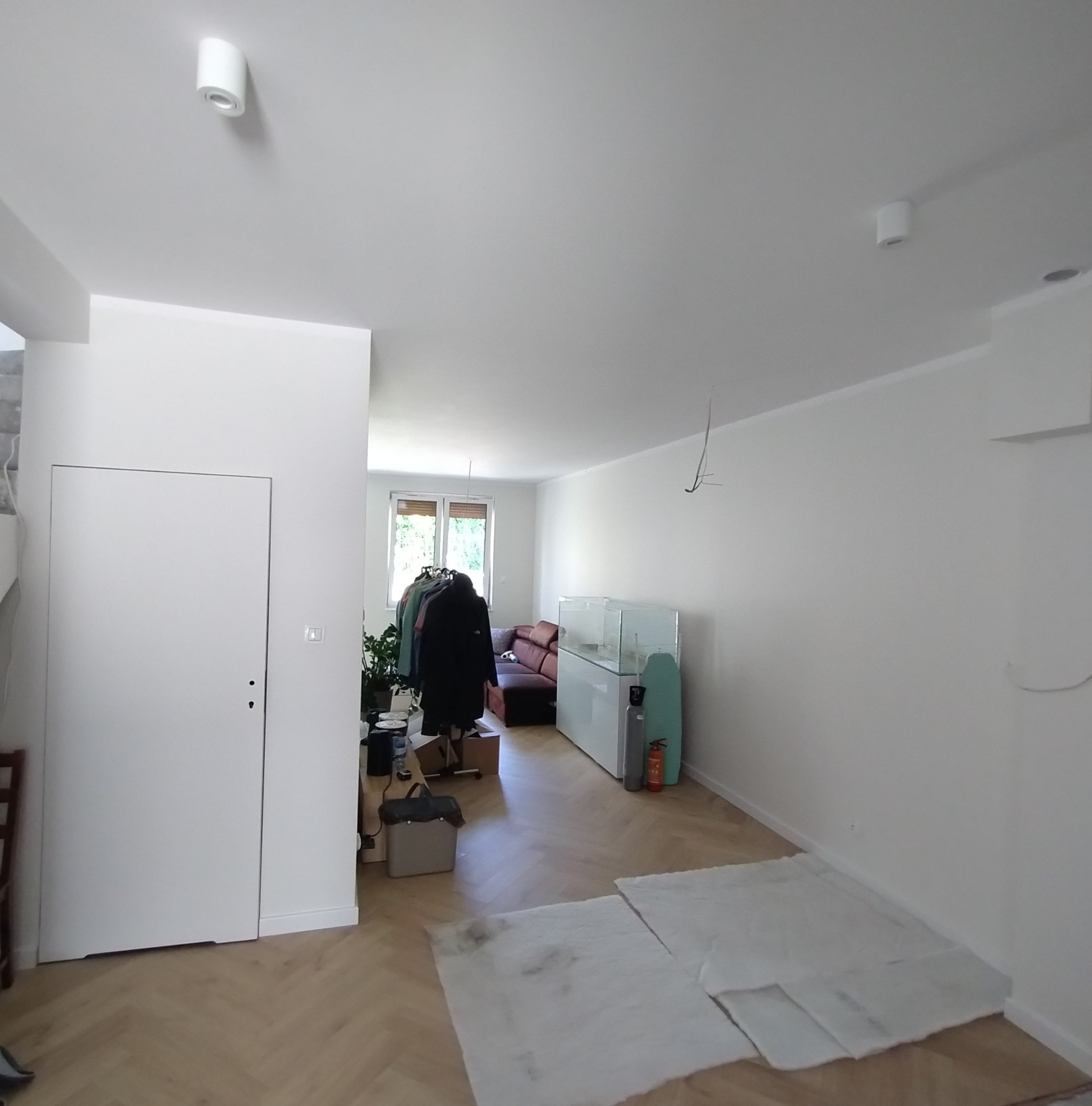 Jasne wnętrze po remoncie z białymi ścianami, parkietem w jodełkę i minimalistycznym oświetleniem. Widoczne przygotowania do dalszych prac wykończeniowych.