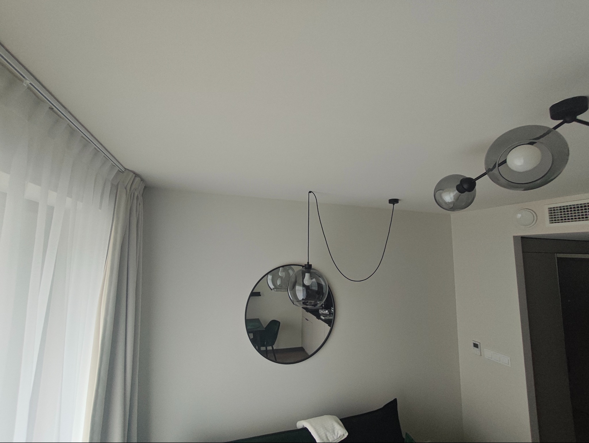 Nowoczesne wykończenie wnętrza: okrągłe lustro na ścianie, designerskie lampy wiszące i sufitowe, minimalistyczne zasłony. Estetyczne detale w jasnym pomieszczeniu.