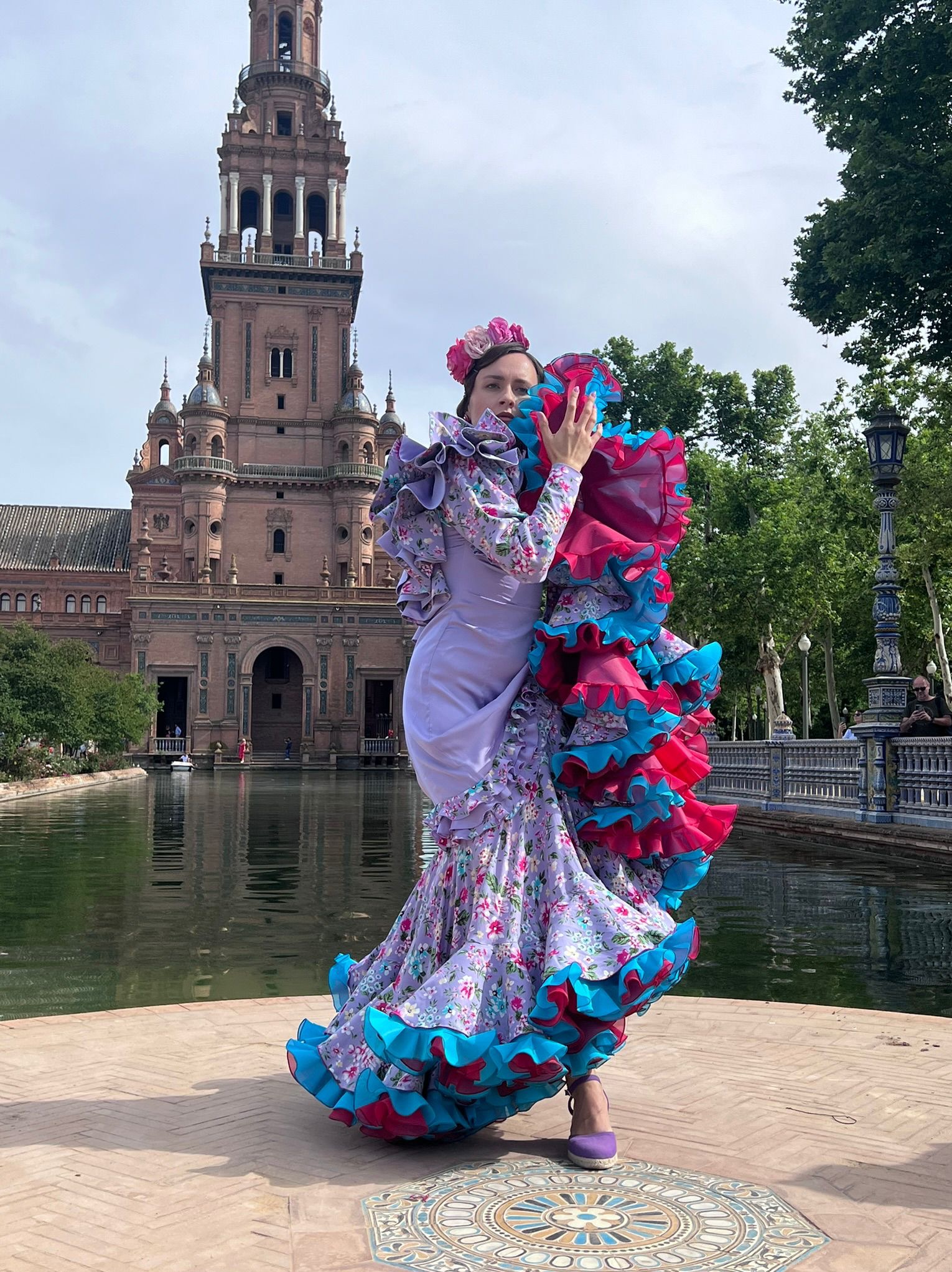 Tancerka flamenco w kwiecistej sukni z falbanami w kolorach różu i turkusu, pozująca na tle Plaza de España w Sewilli.