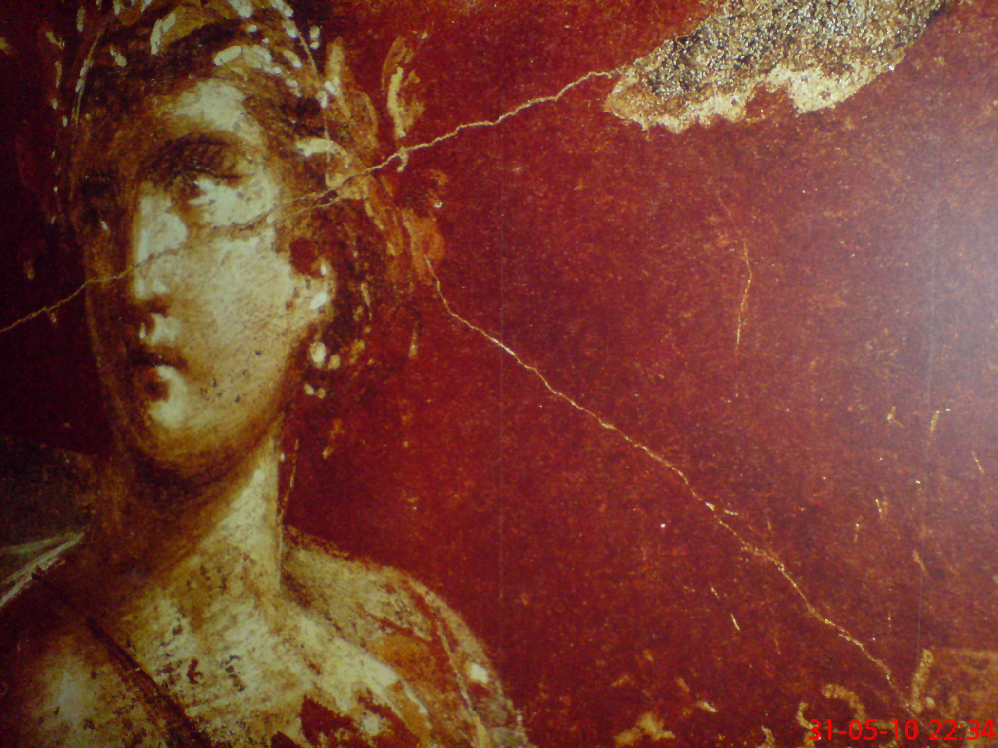 Fragment muralu przedstawiający popiersie kobiety w wieńcu na tle czerwonej, popękanej ściany.