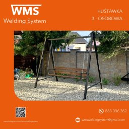 WMS Group Poland Sp. z o.o. - Metalowa huśtawka ogrodowa trzyosobowa z drewnianym siedziskiem na tle kamiennego muru i ogrodu, prezentacja firmy WMS Welding System.