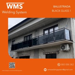 WMS Group Poland Sp. z o.o. - Balkon z czarną, szklaną balustradą na tle szarej elewacji budynku, widoczne okna i klimatyzator. Zdjęcie zrobione w pochmurny dzień.