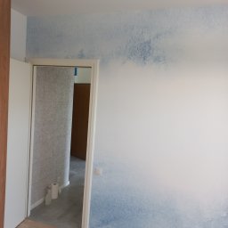 Oleg FENYAK - Pokój po malowaniu z efektem ombre w odcieniach błękitu, widoczne gniazdka elektryczne i fragment łazienki z szarą glazurą w tle.