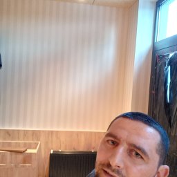 Oleg FENYAK - Ściana w jasne pionowe pasy po remoncie, widoczny grzejnik i lampy sufitowe, selfie wykonawcy z bliska.