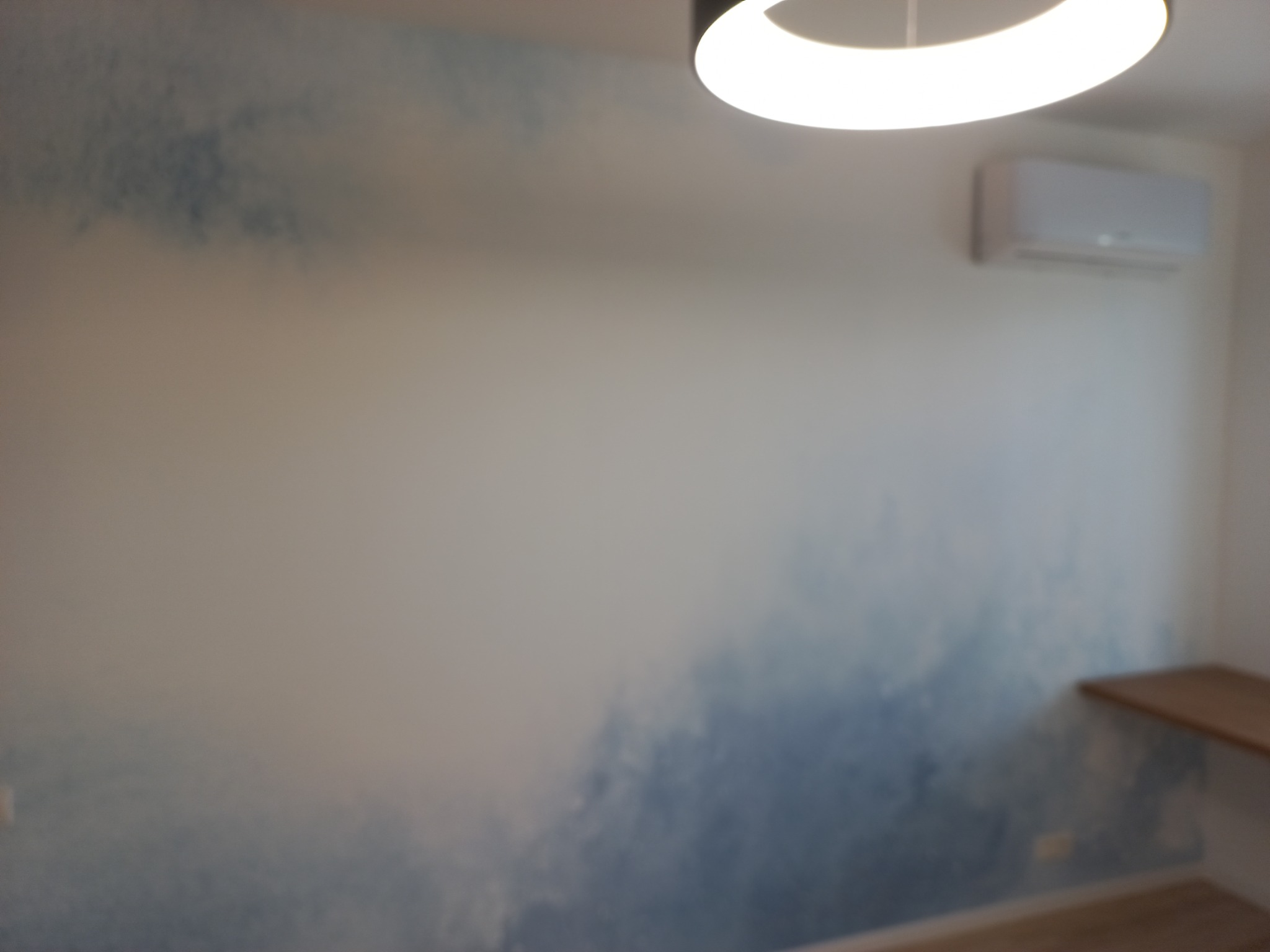 Ściana w pokoju z efektem malarskim przypominającym chmury, oświetlona okrągłą lampą sufitową i z zamontowanym klimatyzatorem.