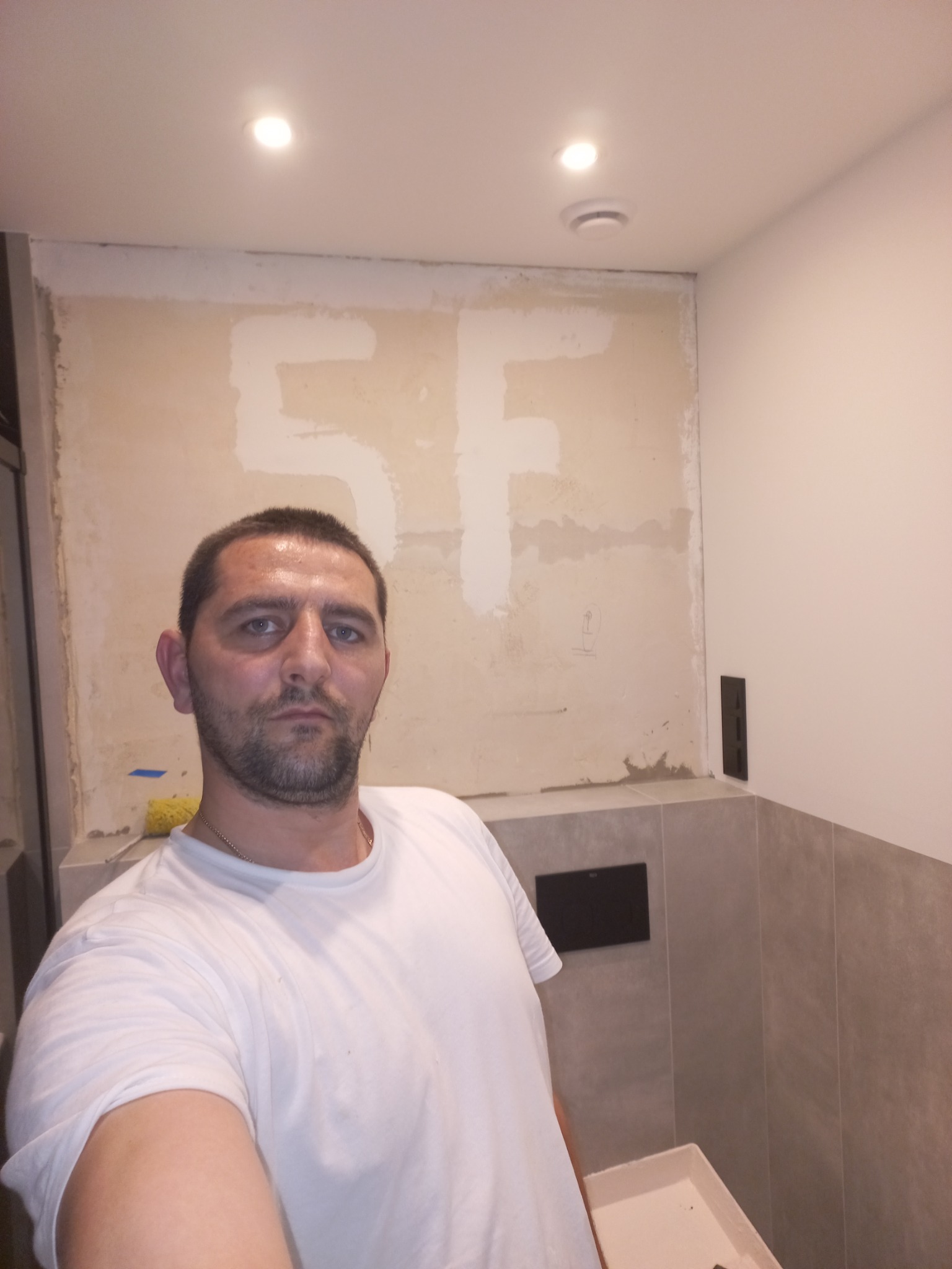 Mężczyzna robiący selfie na tle ściany w trakcie prac w łazience w Piasecznie, widoczne ślady po szpachlowaniu i częściowo położone płytki.