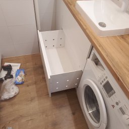 Marek Prządka - Łazienka w trakcie montażu: wysunięta szuflada pod umywalką z blatem drewnopodobnym, obok pralka, na podłodze narzędzia i resztki opakowań.