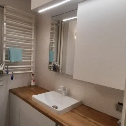 Marek Prządka - Nowoczesna łazienka z zabudową meblową: białe szafki wiszące, drewniany blat z umywalką nablatową i pralką w zabudowie.