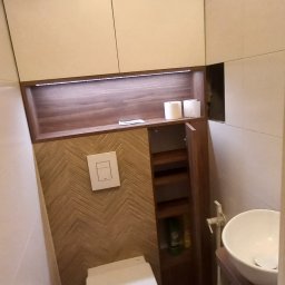 Marek Prządka - Nowoczesna toaleta z zabudową meblową: szafki wiszące, półki z oświetleniem LED, ściana wykończona drewnopodobną mozaiką w jodełkę, umywalka nablatowa.