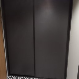 Marek Prządka - Dwudrzwiowa szafa wnękowa z czarnymi, przesuwnymi drzwiami na tle podłogi w czarno-białe wzory geometryczne.