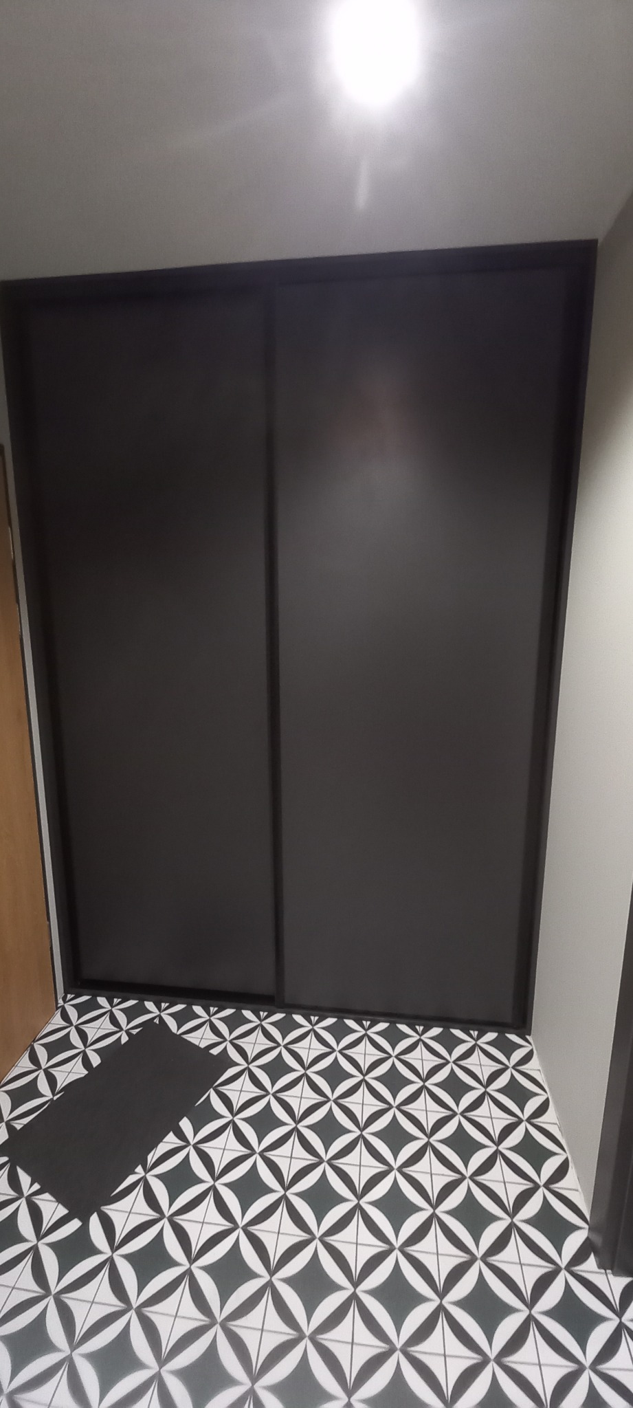 Dwudrzwiowa szafa wnękowa z czarnymi, przesuwnymi drzwiami na tle podłogi w czarno-białe wzory geometryczne.