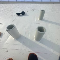 PRO-BUD DANIEL BOŁOTOW - Montaż rur wentylacyjnych na białej membranie dachowej, widoczne zaznaczone obrysy, narzędzia pracy i fragment dachu szklarni w tle.