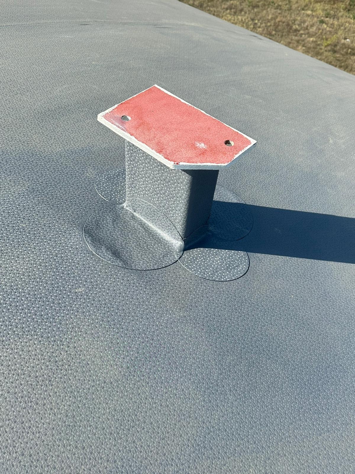 Szary zbiornik z metalową podstawą i czerwoną płytką na górze, widoczne ślady spawania i cień