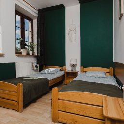 KPCEEiS GRZEGORZ WĄS - Pokój z dwoma drewnianymi łóżkami w Bydgoszczy, zielono-białe ściany, dekoracje w stylu skandynawskim, radio na szafce nocnej, widok z okna.
