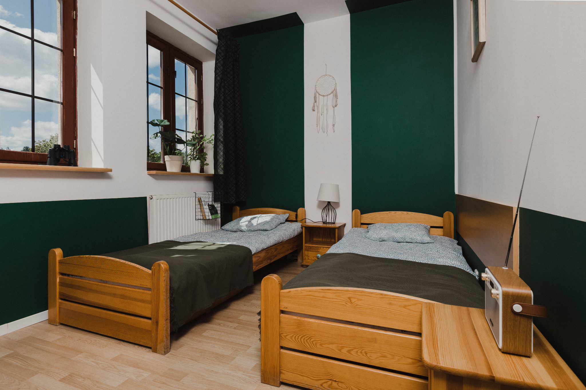 Pokój z dwoma drewnianymi łóżkami w Bydgoszczy, zielono-białe ściany, dekoracje w stylu skandynawskim, radio na szafce nocnej, widok z okna.