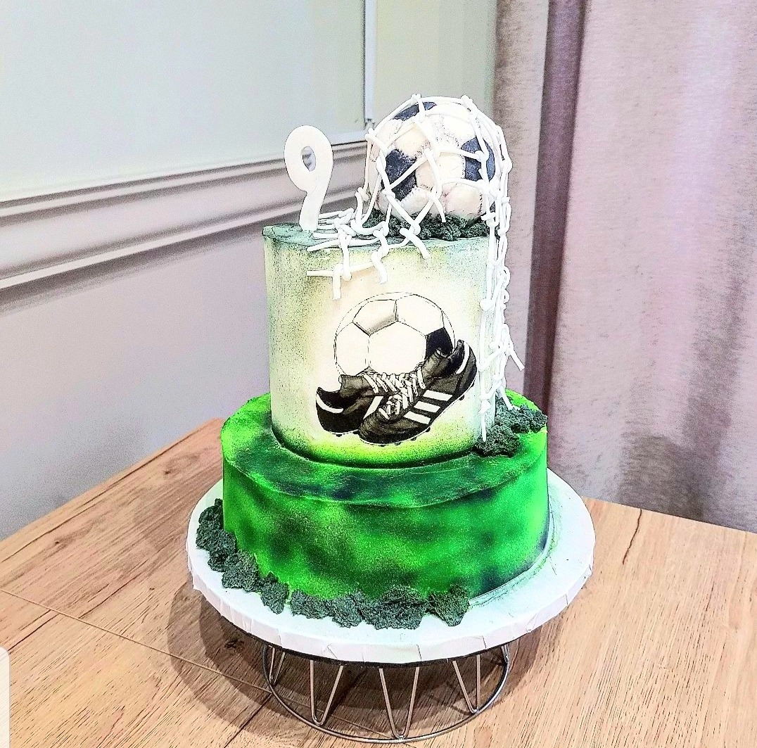 Dwupoziomowy tort urodzinowy z motywem piłkarskim, dekorowany piłką w siatce, butami piłkarskimi i cyfrą '9' na wierzchu.