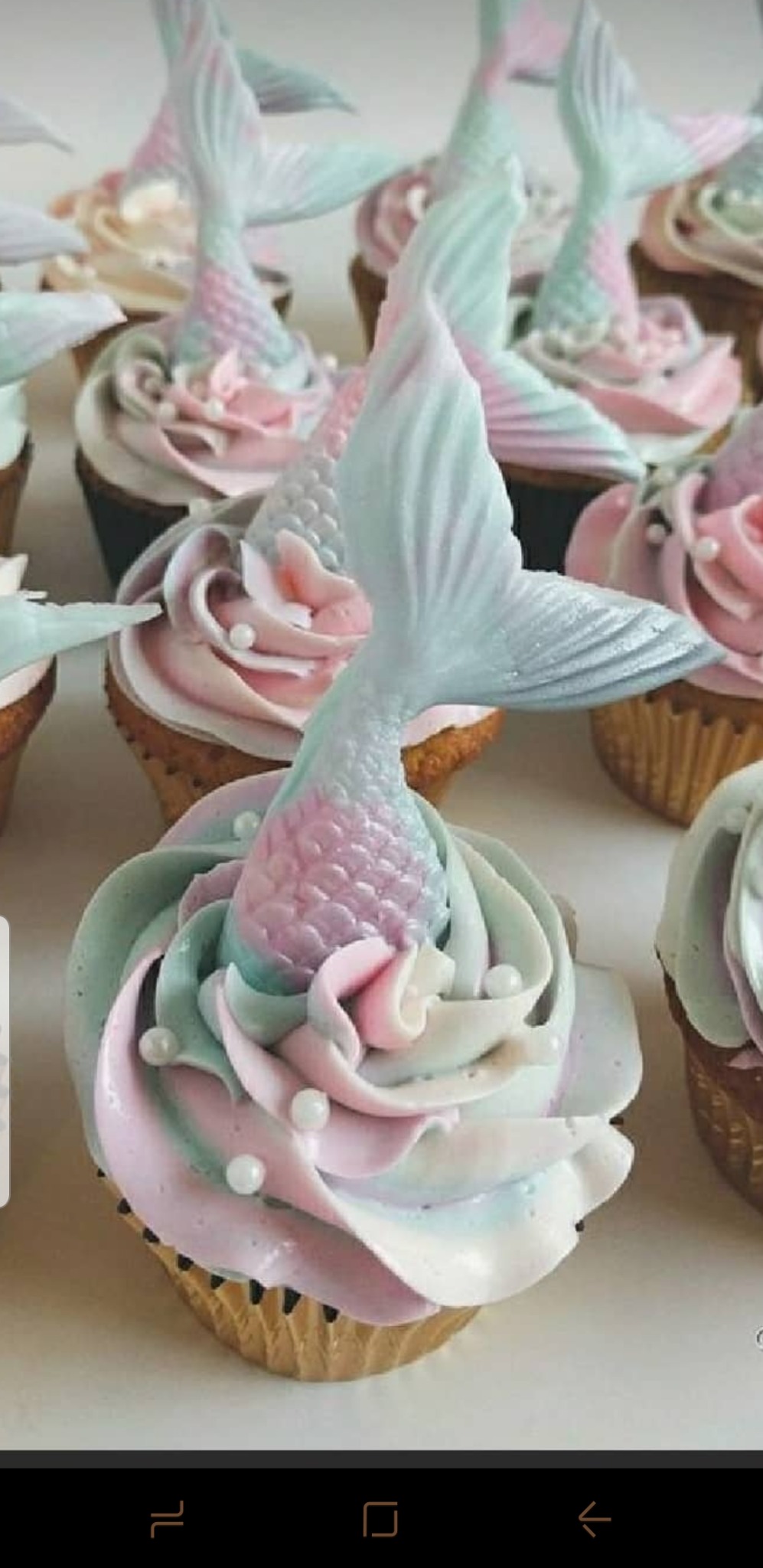 Kolekcja babeczek z kremem w pastelowych odcieniach i dekoracjami w kształcie ogonów syren, ozdobione drobnymi, białymi perełkami.