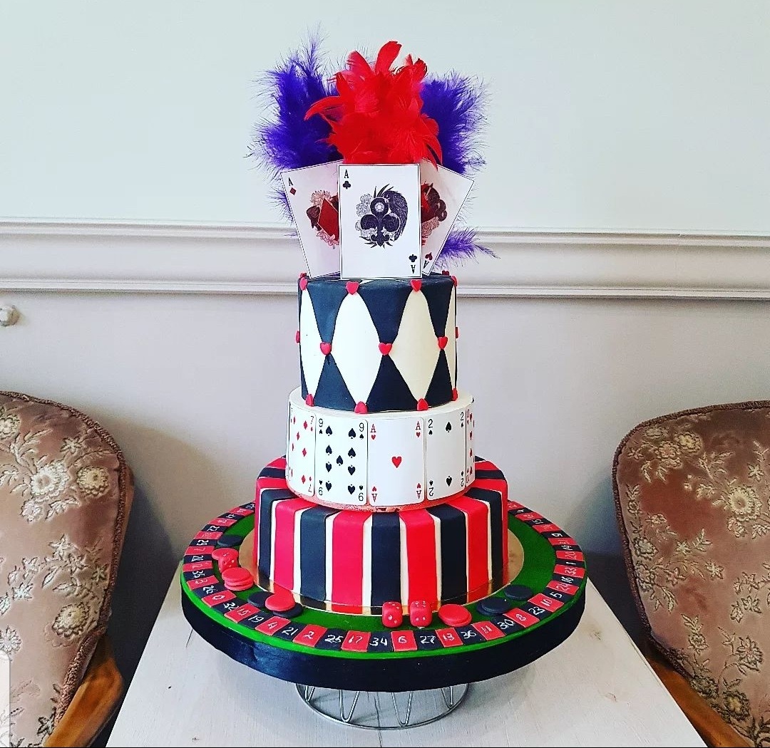 Wielopoziomowy tort z motywem kasyna: ruletka, karty do gry i pióra w kolorach czerwonym i fioletowym.