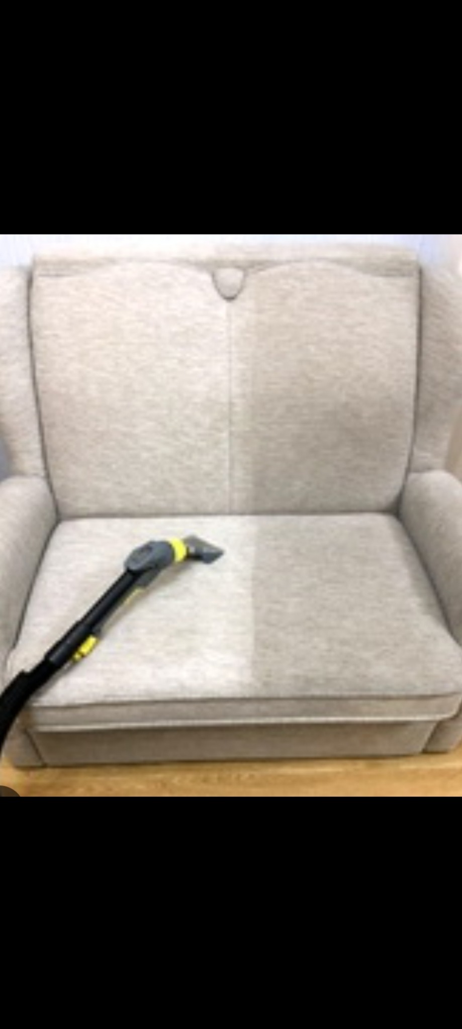 Jasnoszary fotel z widoczną różnicą w czystości tapicerki po praniu, z użyciem czarnego odkurzacza piorącego z żółtymi elementami.