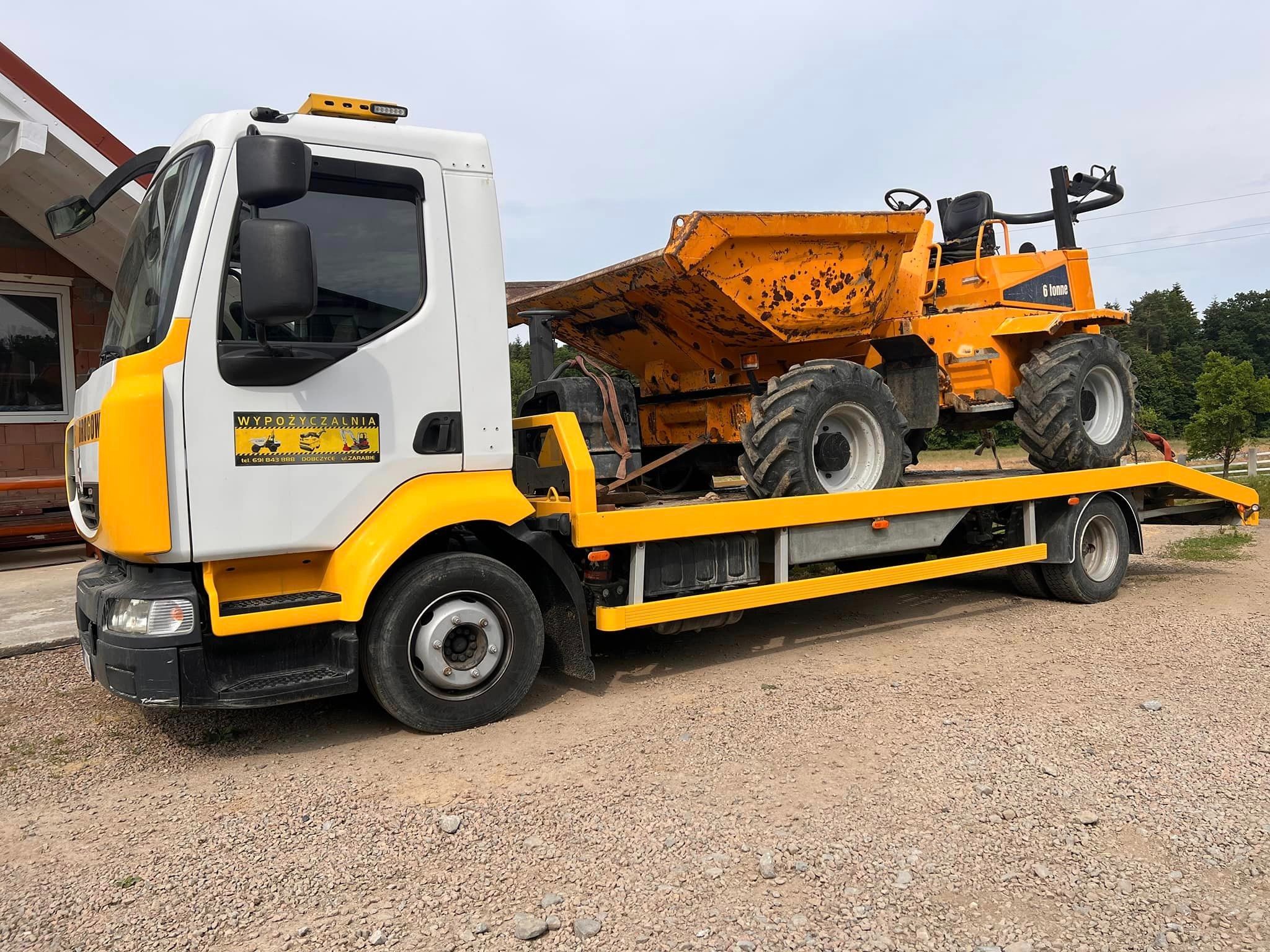 Laweta z żółtymi elementami transportuje pomarańczową, brudną wywrotkę budowlaną 6 tonne na żwirowej powierzchni w słoneczny dzień.