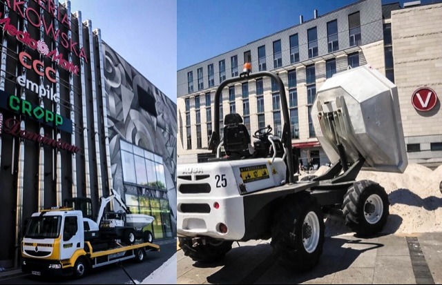 Żółto-biała laweta z małą wywrotką na platformie, zaparkowana przed budynkiem galerii handlowej, oraz wywrotka AUSA 25 wysypująca piasek na placu miejskim.