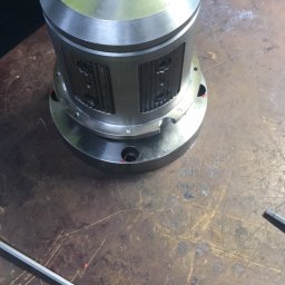 Industrial Service - Metalowa obudowa cylindryczna z otworami, dokręcana kluczem imbusowym nasadowym na stole roboczym z widocznymi śladami użytkowania, w tle ręka w niebieskiej rękawicy roboczej i fragment odzieży...