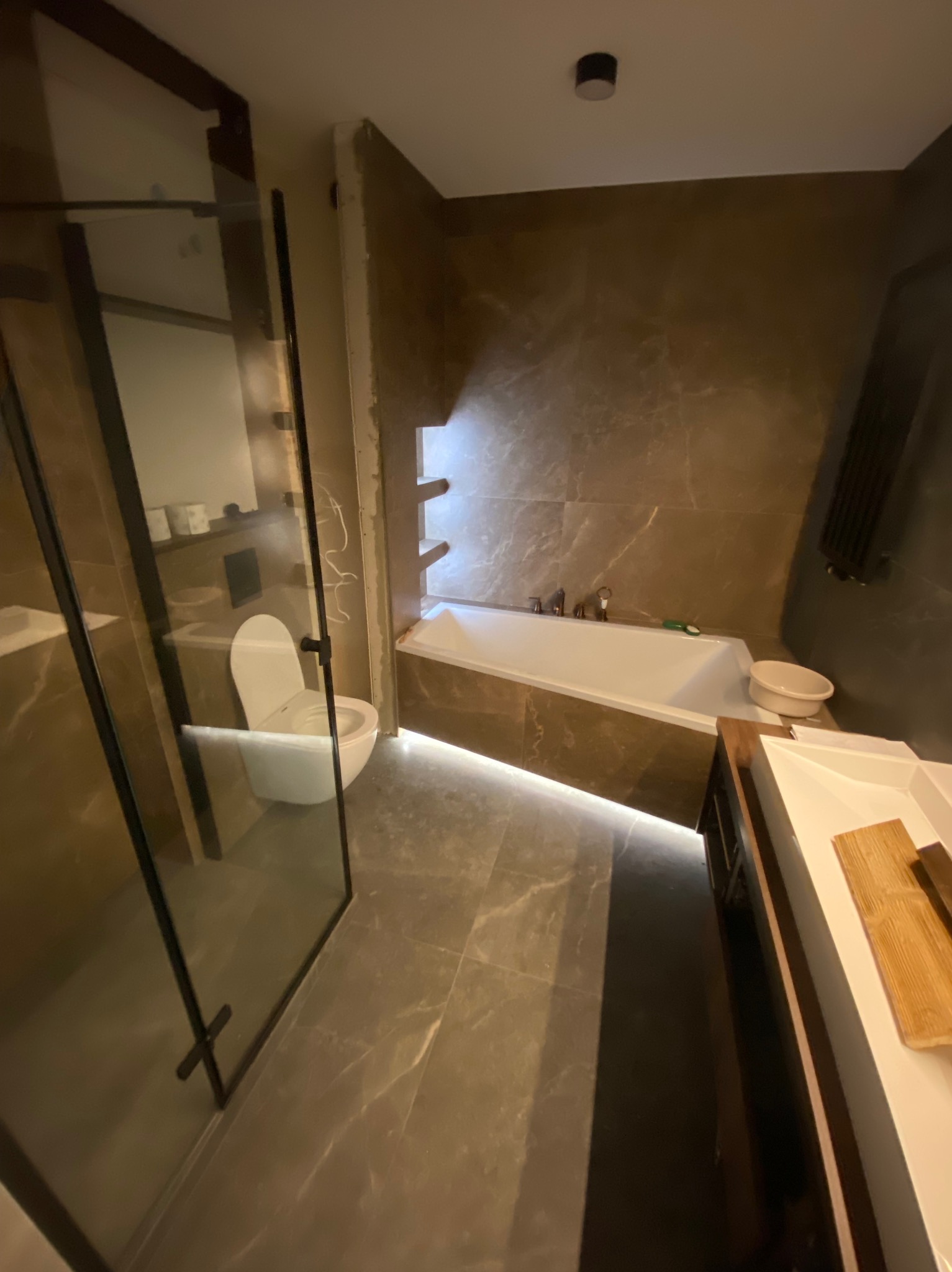 Nowoczesna łazienka w trakcie wykańczania z podświetlaną wanną, kabiną prysznicową z czarnymi ramami i toaletą, widoczne niedokończone fragmenty ścian.