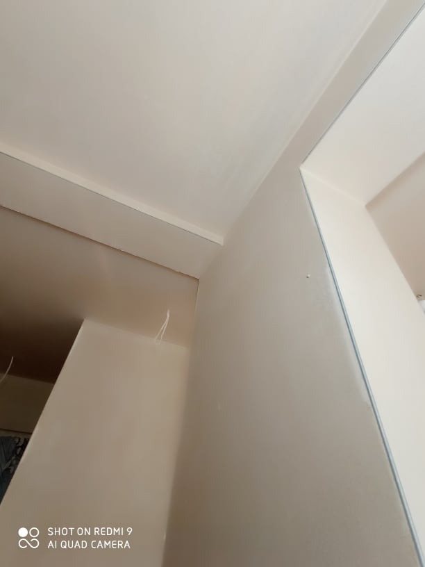 Świeżo otynkowany narożnik wewnętrzny pomieszczenia z widocznymi przewodami wystającymi ze ściany, jasne, jednolite wykończenie.