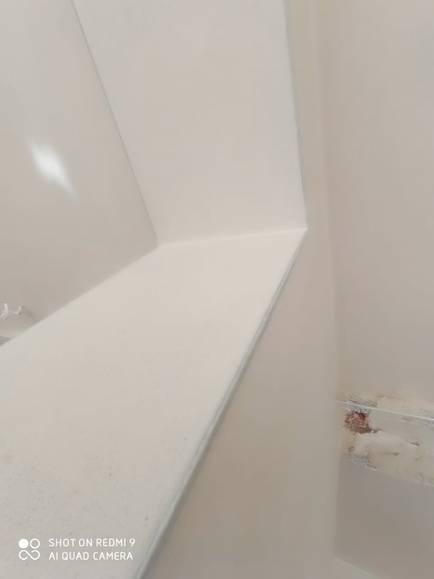 Świeżo położone, gładkie tynki na styku ściany i sufitu, widoczne delikatne refleksy światła, zabezpieczone fragmenty instalacji pod sufitem.