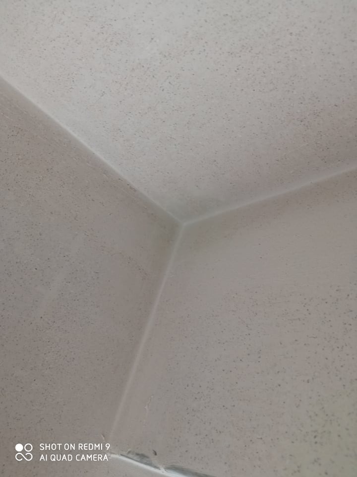 Szara, chropowata powierzchnia ściany i sufitu w rogu pomieszczenia, z delikatnym efektem ziarnistości.