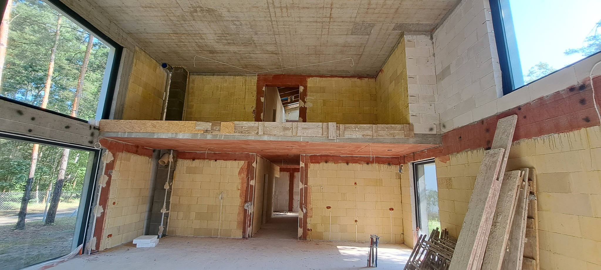 Surowy stan wnętrza domu w Warszawie przed tynkowaniem, z widocznymi bloczkami i instalacjami, dwukondygnacyjny, z dużymi oknami.