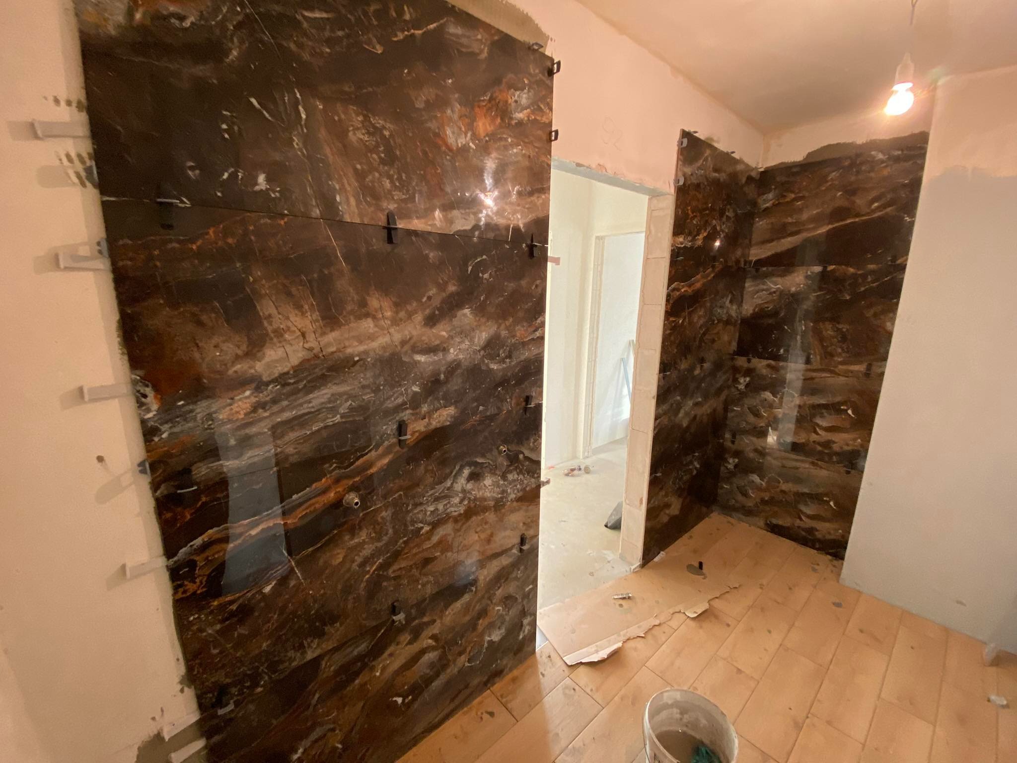 Montaż płytek imitujących marmur na ścianie łazienki, widoczne klipsy dystansowe i wiadro na podłodze, surowy stan wykończenia.