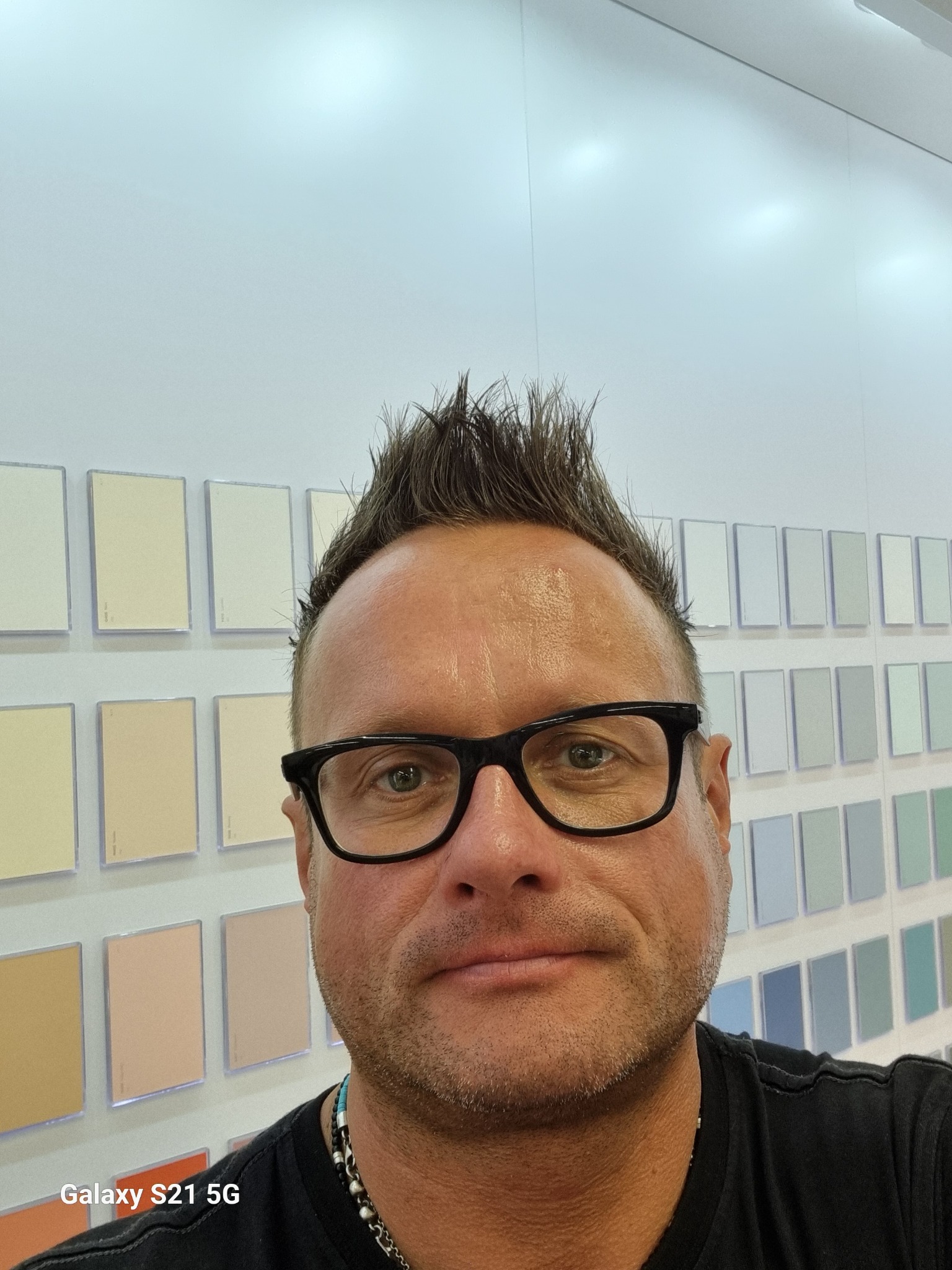 Mężczyzna w okularach na tle ściany z próbkami kolorów farb do malowania mieszkań.