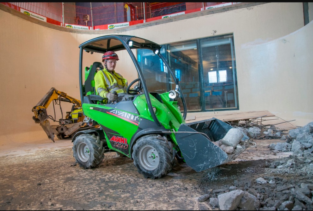 Operator w kasku i kamizelce odblaskowej obsługuje zieloną mini-ładowarkę Avant 225, zbierając gruz wewnątrz okrągłego budynku w trakcie prac rozbiórkowych.