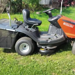 Traktorek do koszenia trawy Oleo-Mac z koszem, stojący na trawniku.